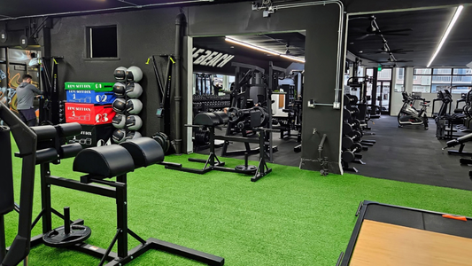 Modern gym with turf flooring, strength machines, and free weights in a black-walled training area.