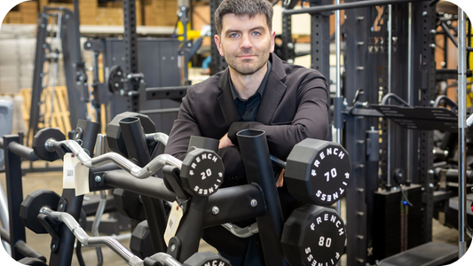 Tim French, founder of Fitness Superstore and French Fitness, standing in a showroom surrounded by commercial gym equipment and branded dumbbells.