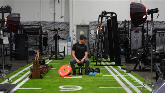 Tim French, CEO &amp; Founder of Fitness &nbsp;Superstore, wearing a black French Fitness T-shirt at Fitness Superstore Benicia showroom surrounded by equipment, including weight plates, kettlebells, dumbbells, and a rowing machine on green turf.