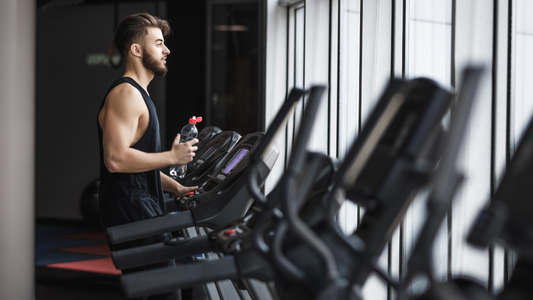 Man standing on a treadmill holding a water bottle, taking a break during a workout in a modern fitness center.